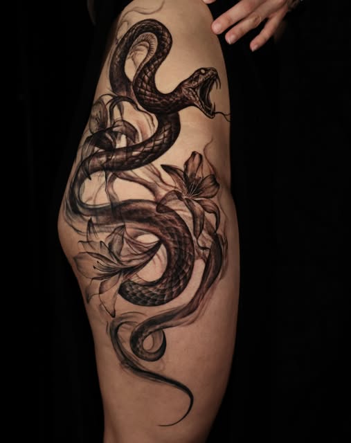 Black and grey snake entwined with lilies tattooed on a thigh