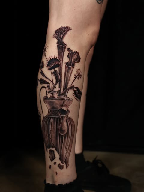 Black and grey carnivorous plant arrangement tattooed on a lower leg